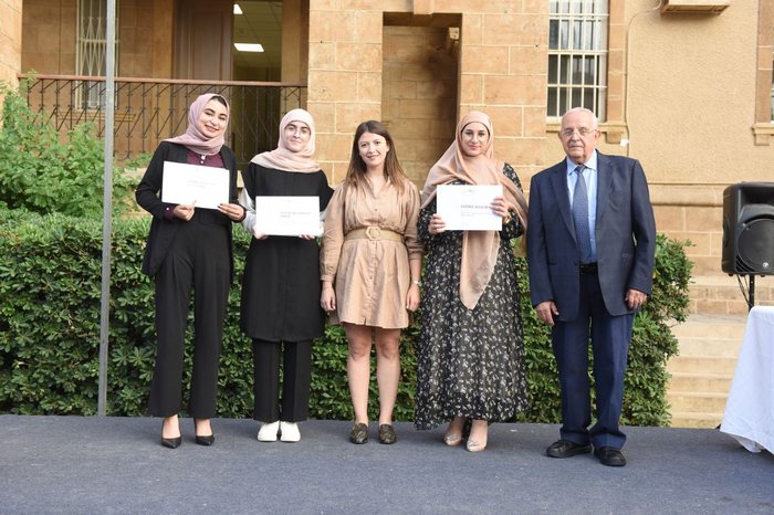 Four award recipients and a presenter holding certificates in a courtyard