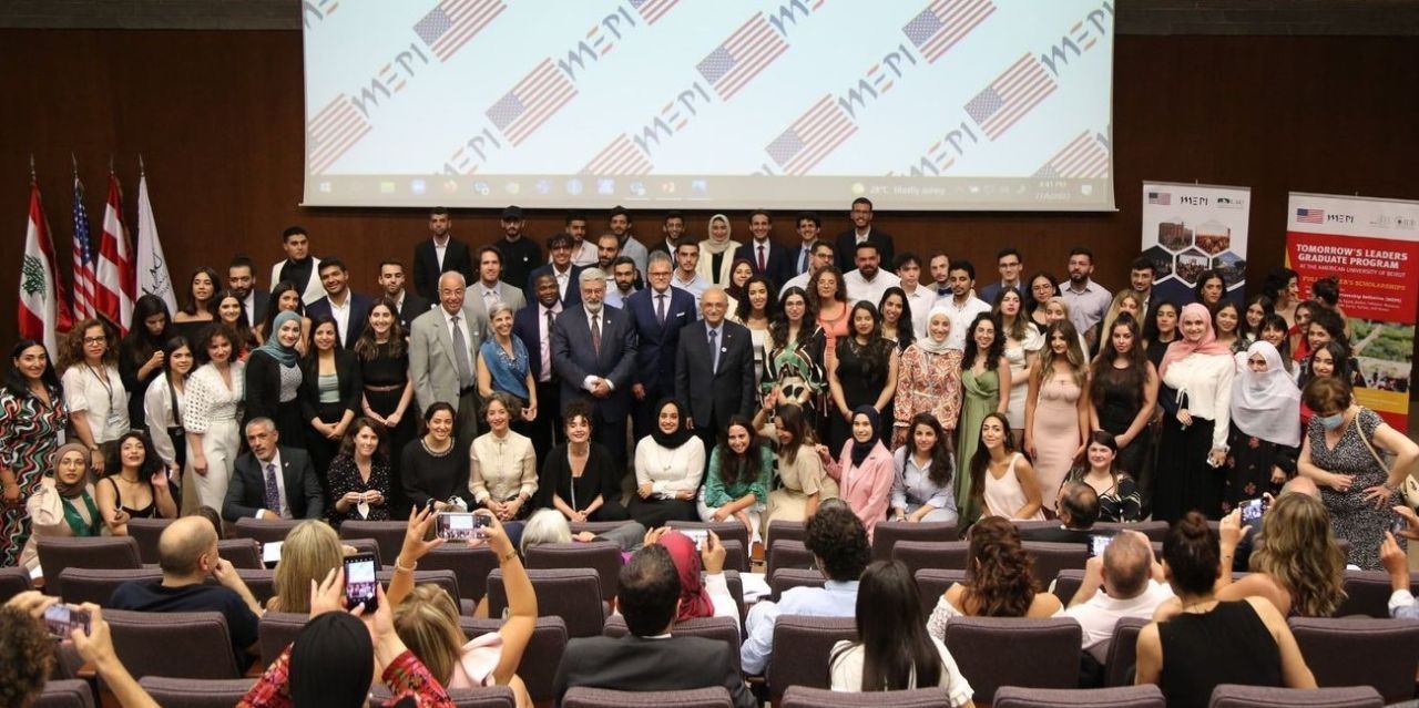 The graduating class and guests posing together on stage in front of a MEPI screen