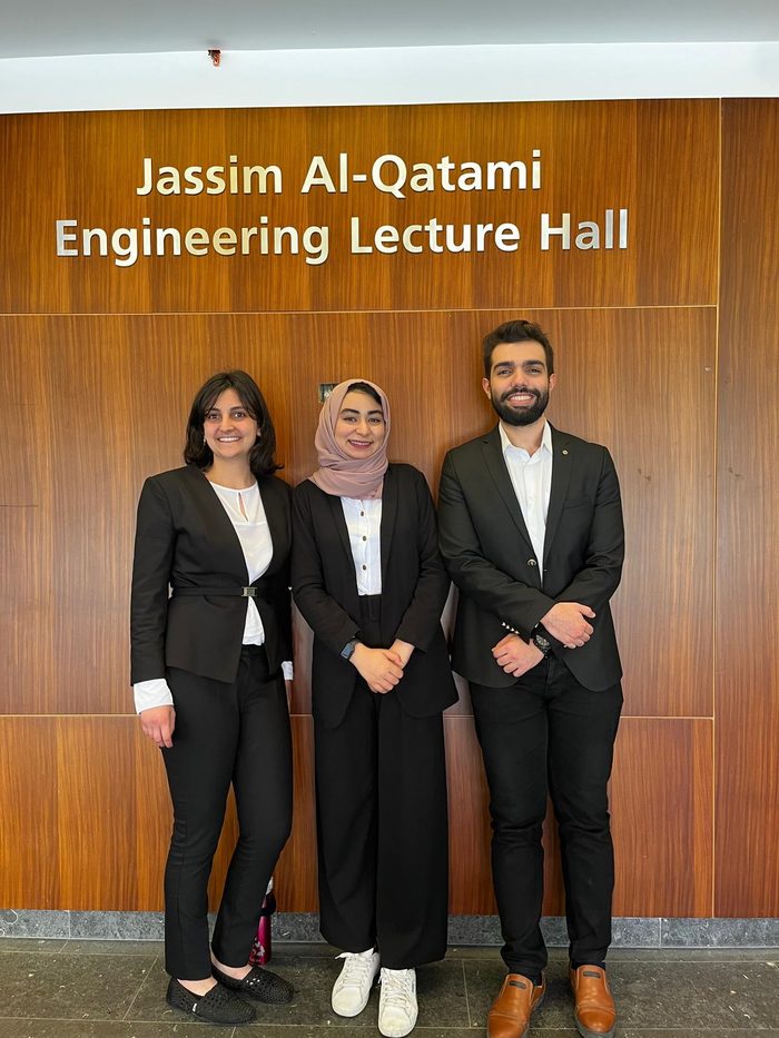 Hadeel with two teammates in front of a lecture hall sign